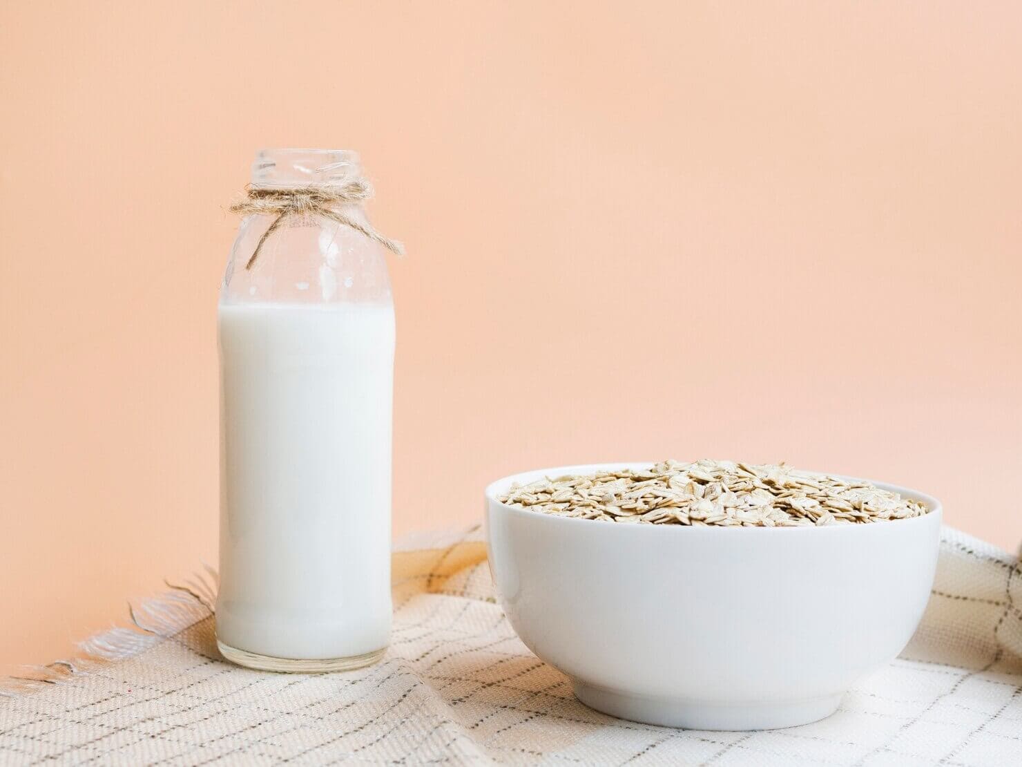 Bottle of oat milk next to a bowl of oats