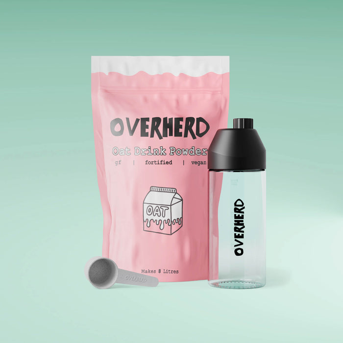 Oat milk powder pouch alongside scoop and glass milk bottle on green gradient background