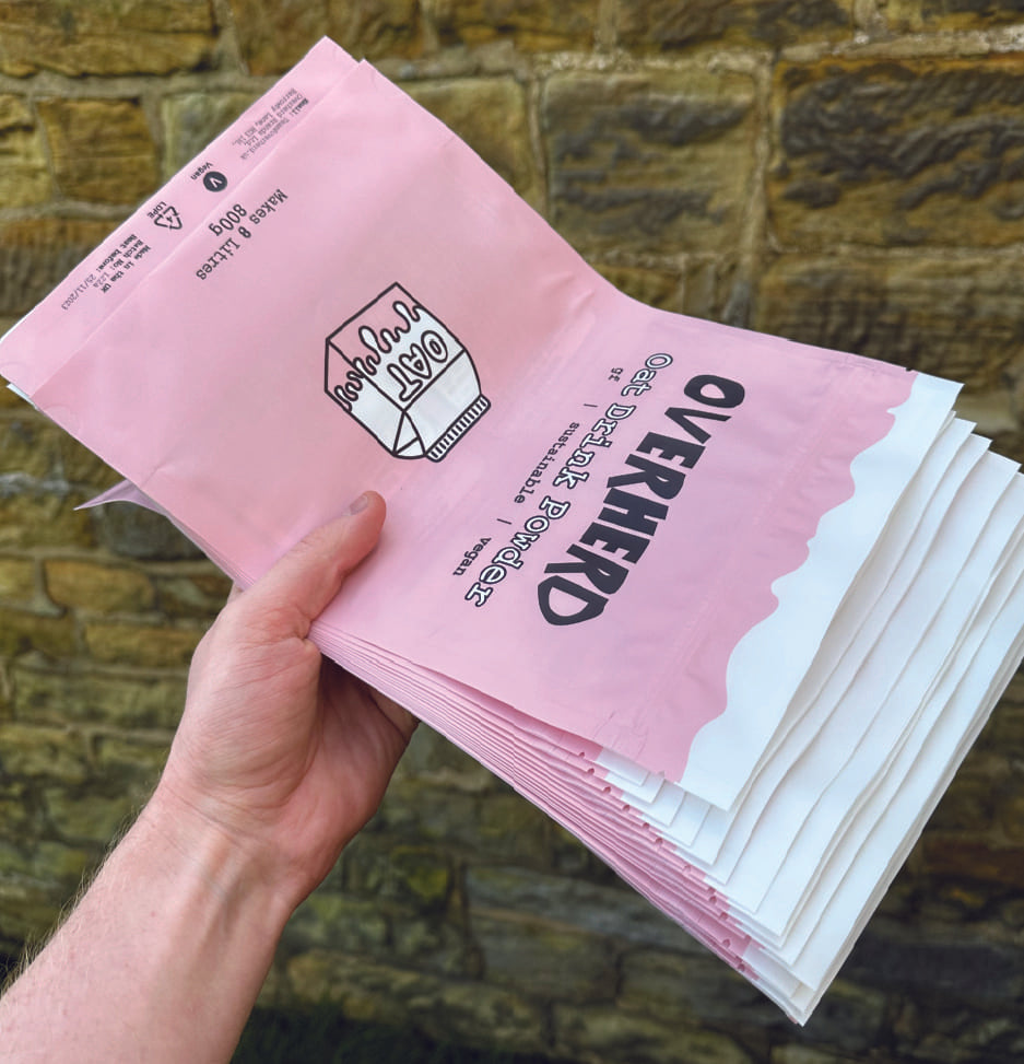 Hand holding a pile of Overherd oat milk powder pouches