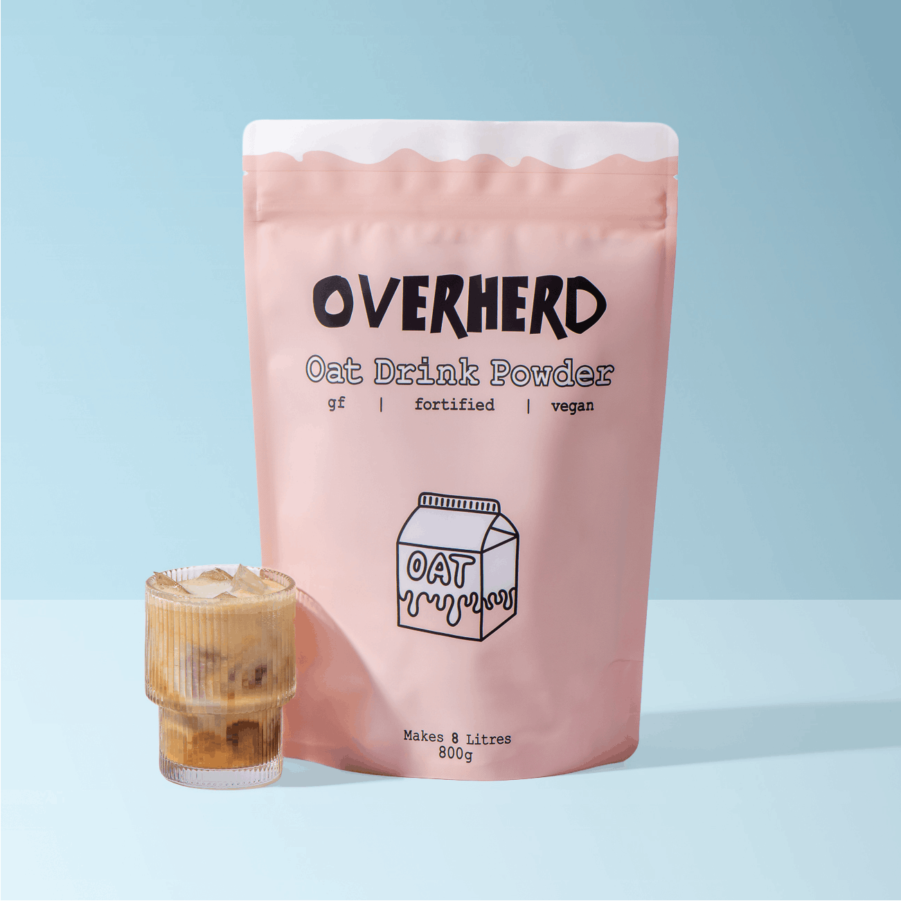 Pouch of Overherd oat milk powder, next to an iced coffee on blue background