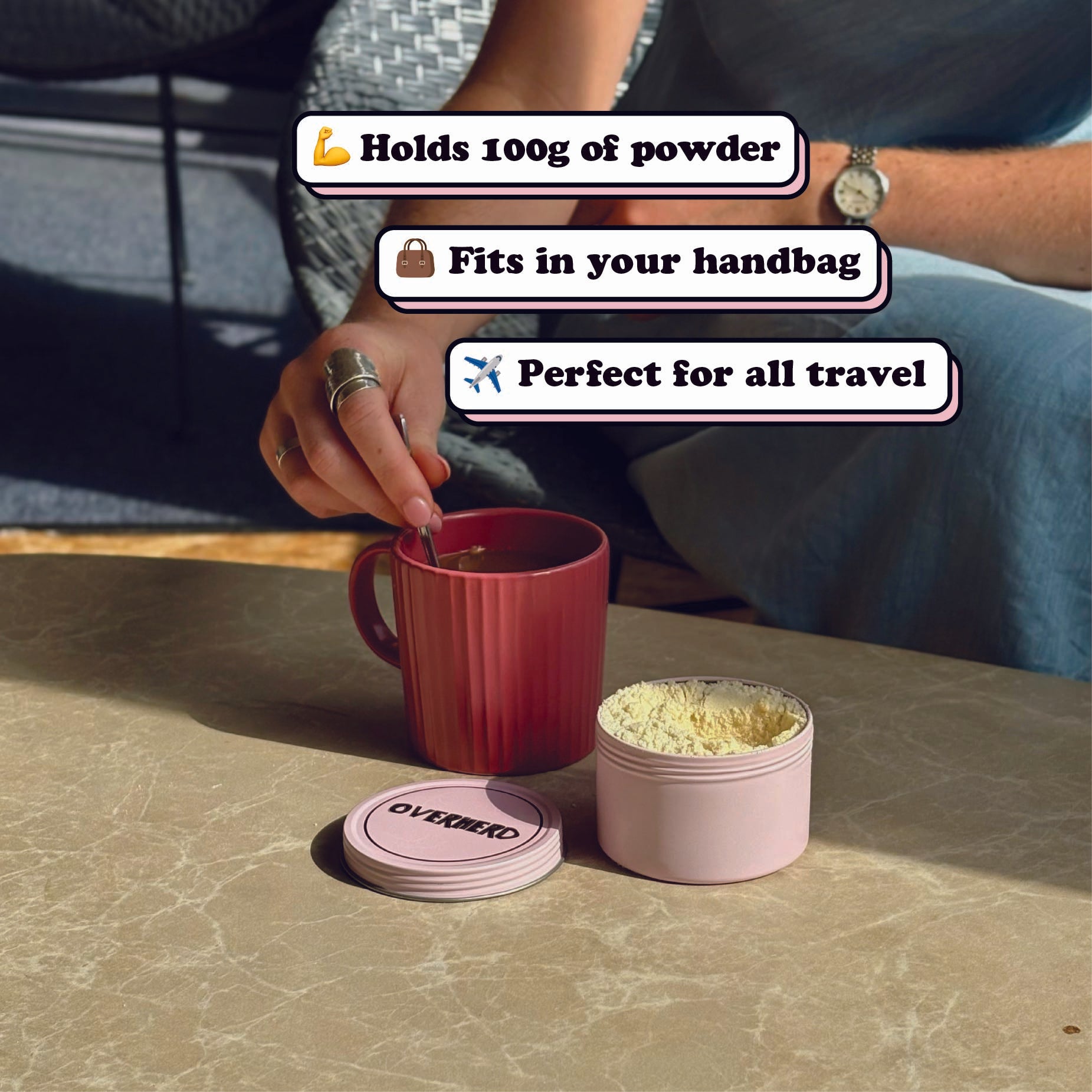Overherd travel tin on a table, alongside a mug of coffee which is being stirred