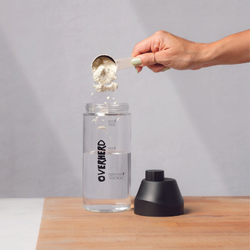 Scooping Overherd oat milk powder into a glass bottle