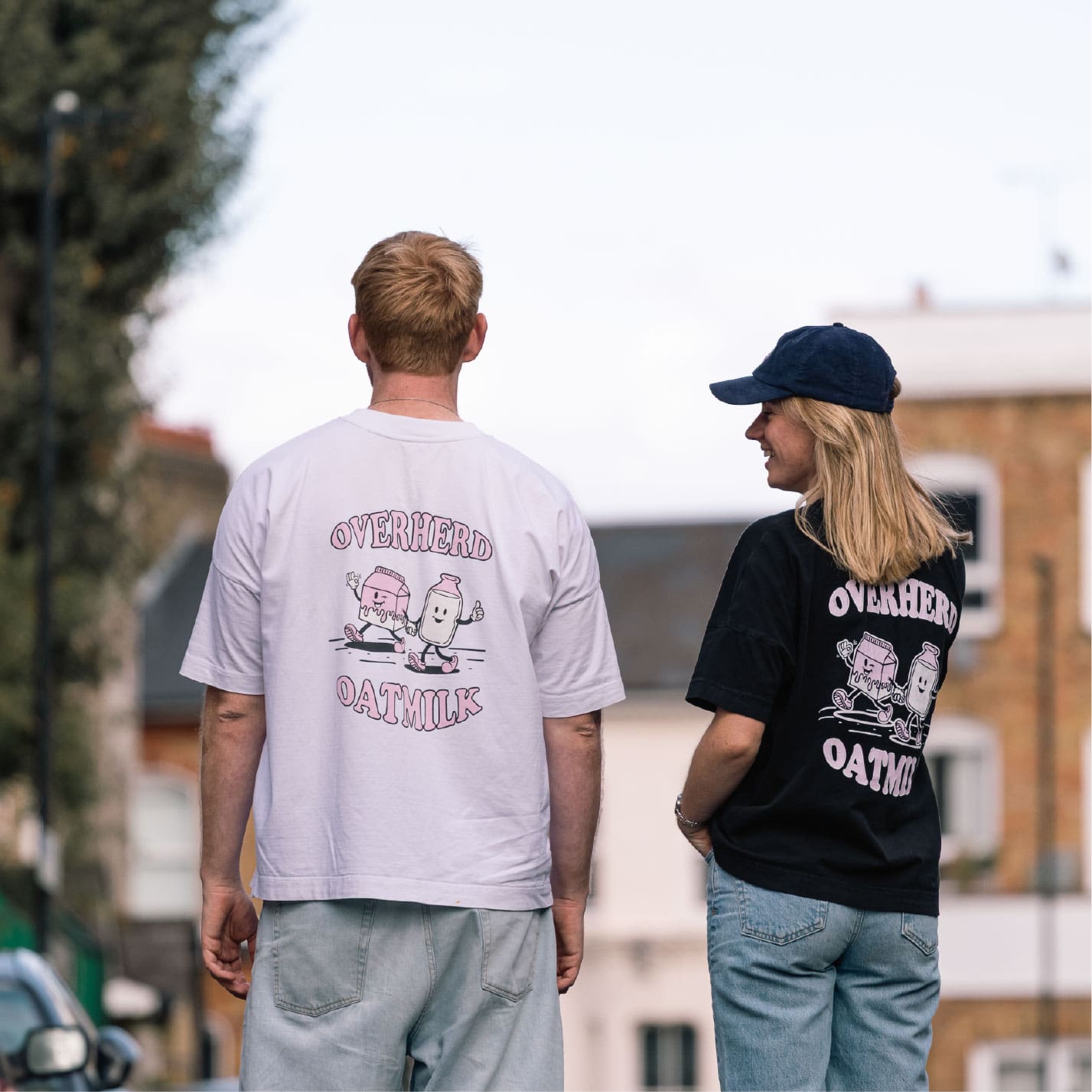 Man and woman standing on a street wearing oat milk t shirts