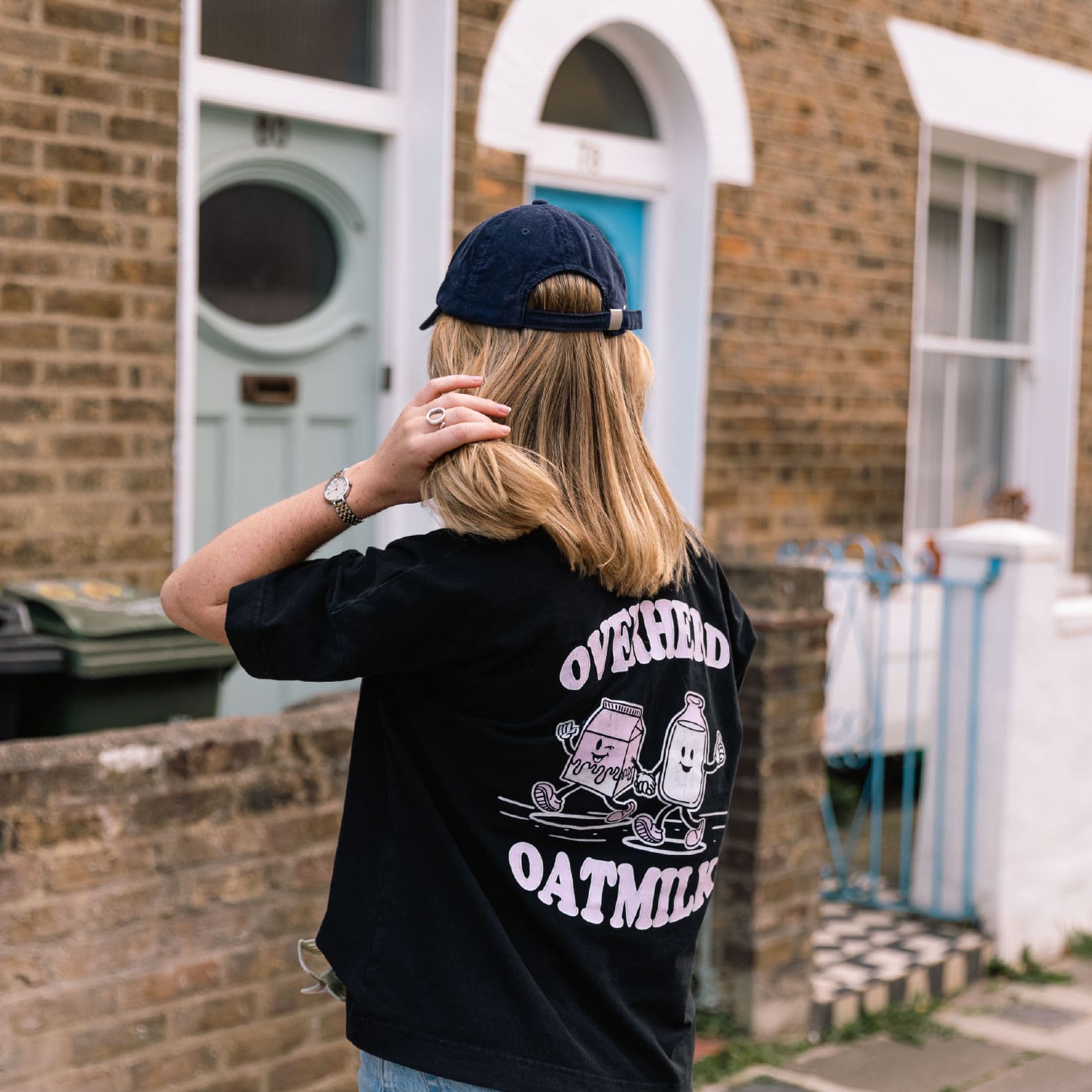 Girl wearing black oat milk t shirt in front of house