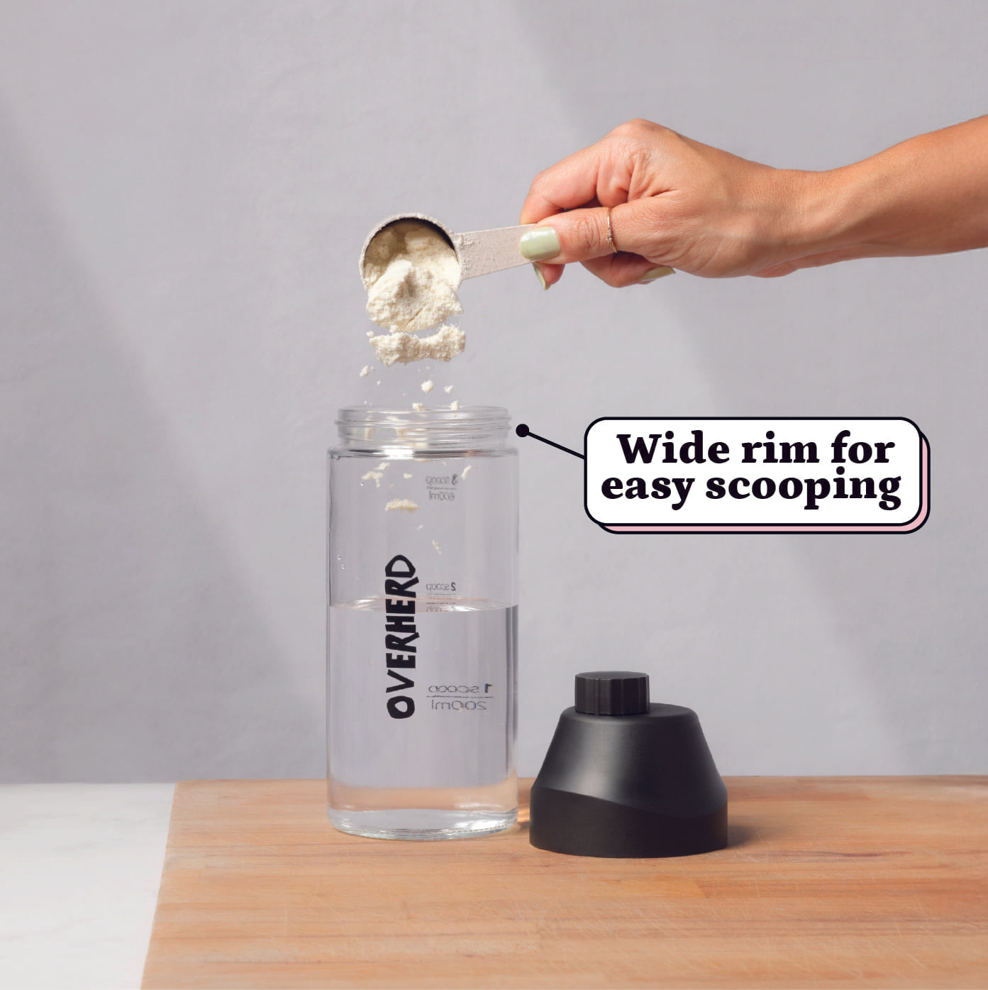 Scooping Overherd oat milk powder into a glass bottle